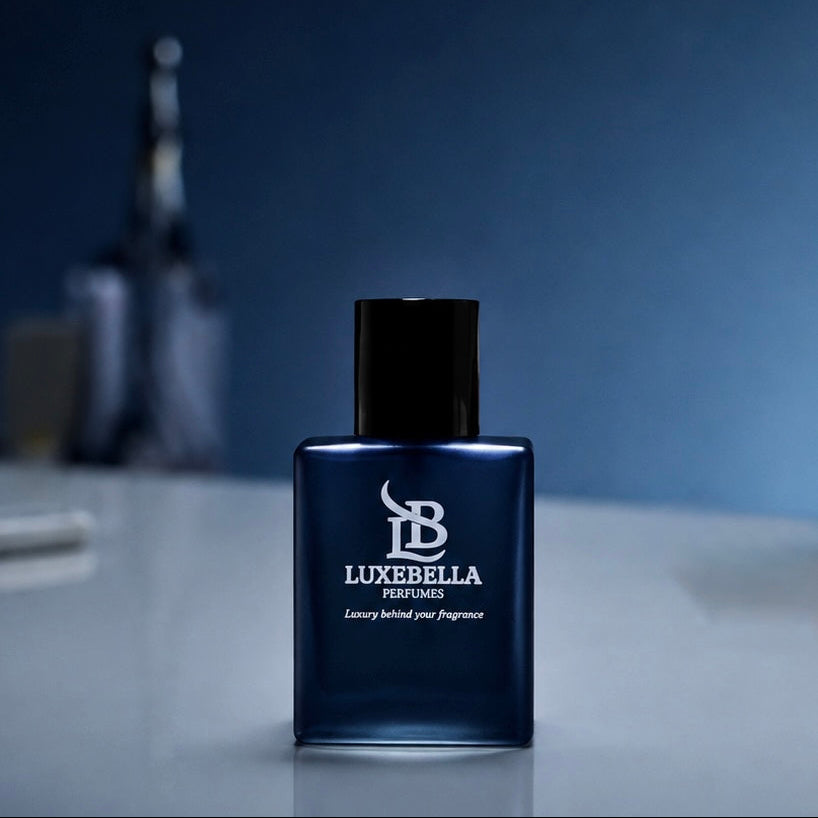 A dark blue rectangular perfume bottle with a black cap, labeled 'LUXEBELLA ESSENCE' and 'Luxury behind your Fragrance', set on a reflective light gray surface against a dark blue gradient background.