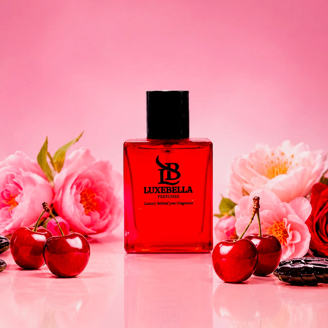 Luxebella Eau de perfume bottle in a vibrant red glass with a black cap, styled on a pink reflective surface with cherries and pink peony flowers.